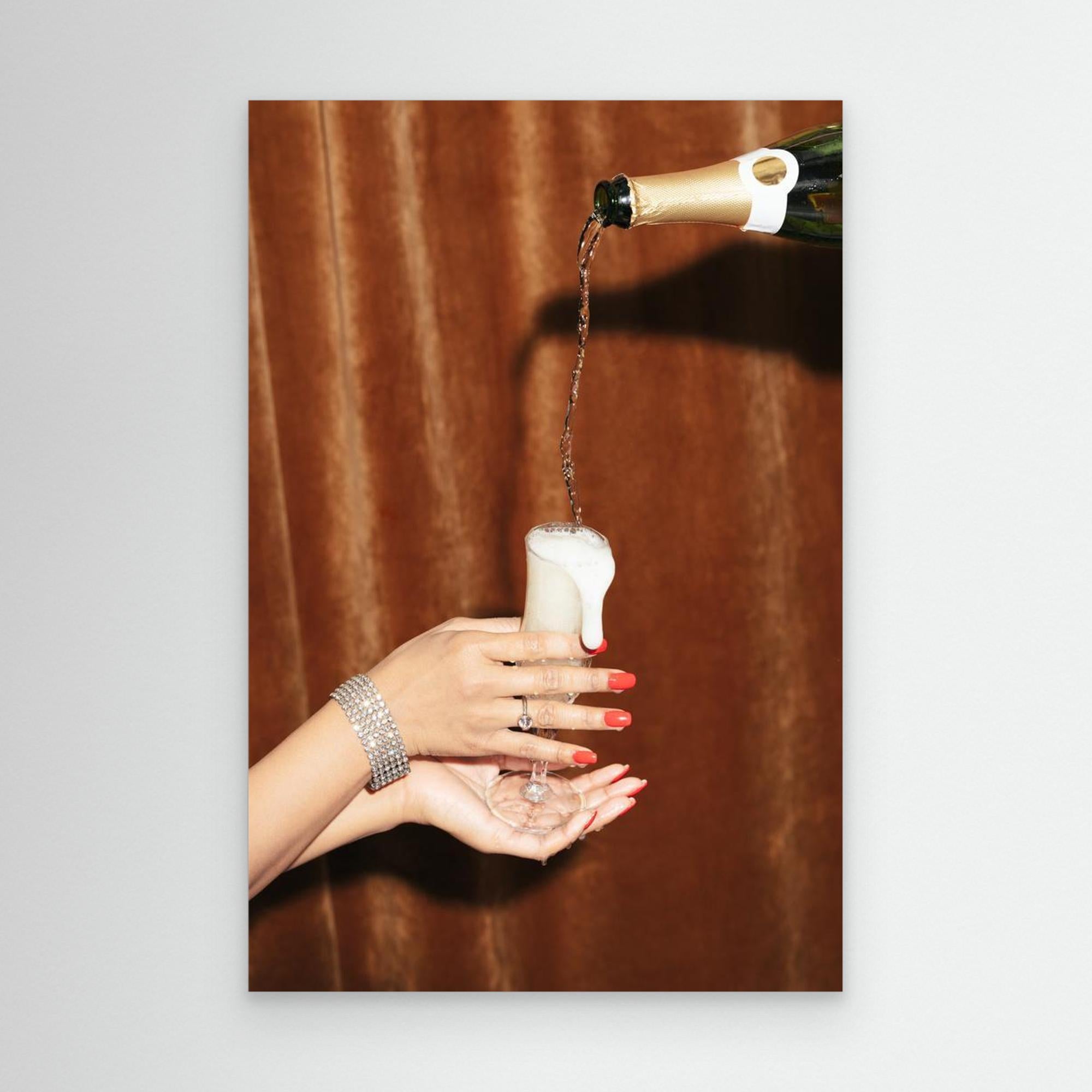 Hand pouring champagne into a glass with a brown curtain background