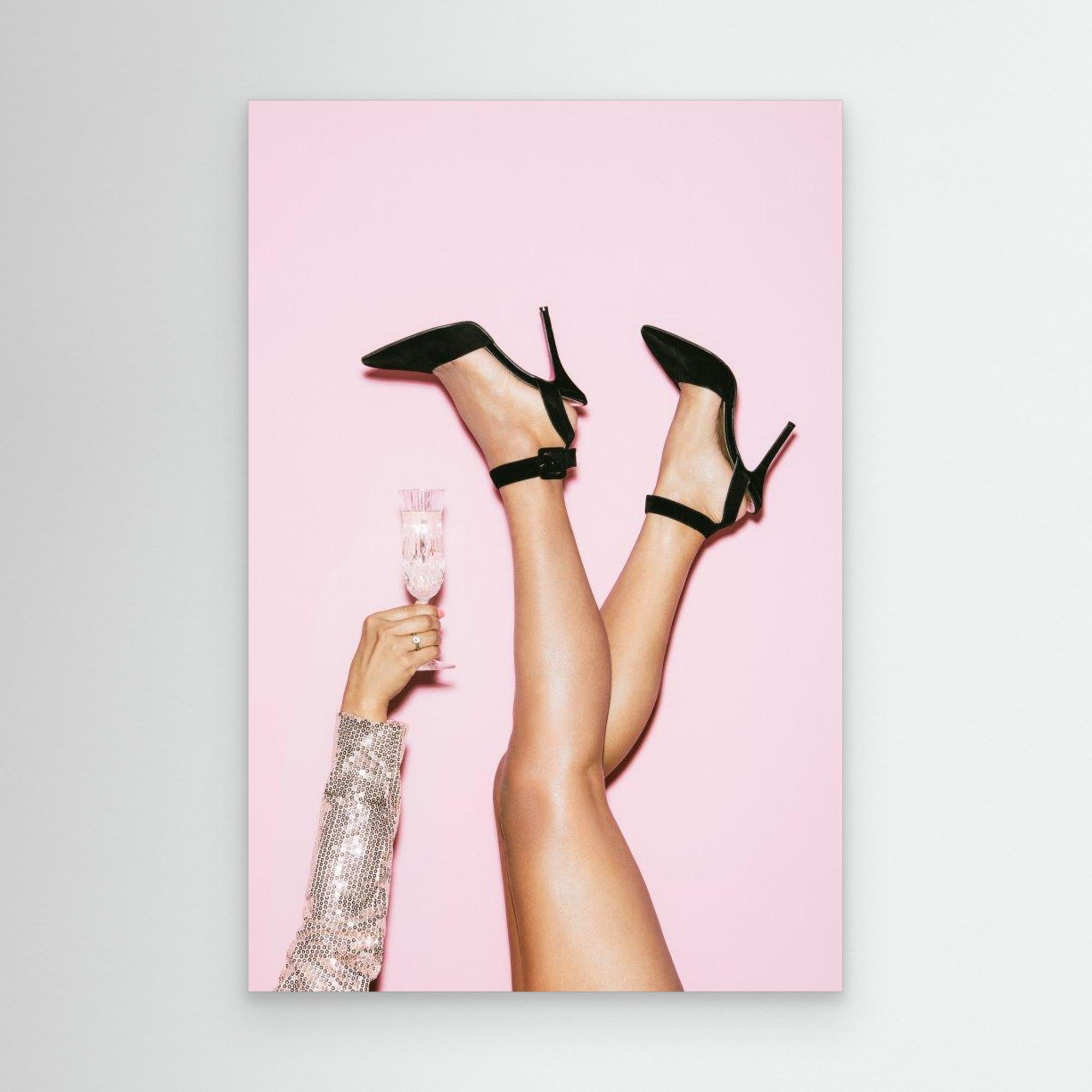 Black high heels on a pink background with a hand holding a glass of champagne.