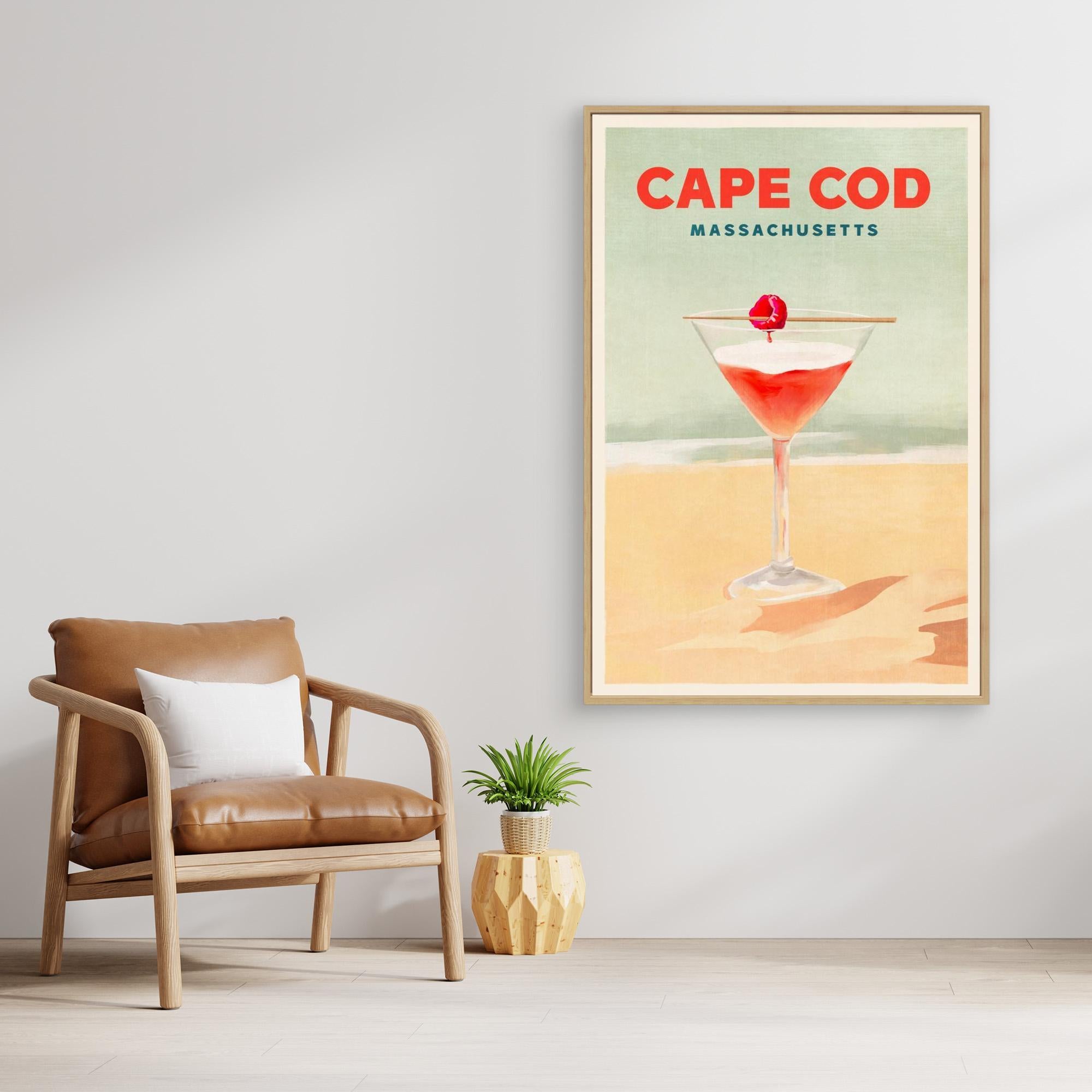 Framed artwork of a cocktail with 'Cape Cod Massachusetts' text in a room with a chair and plant.